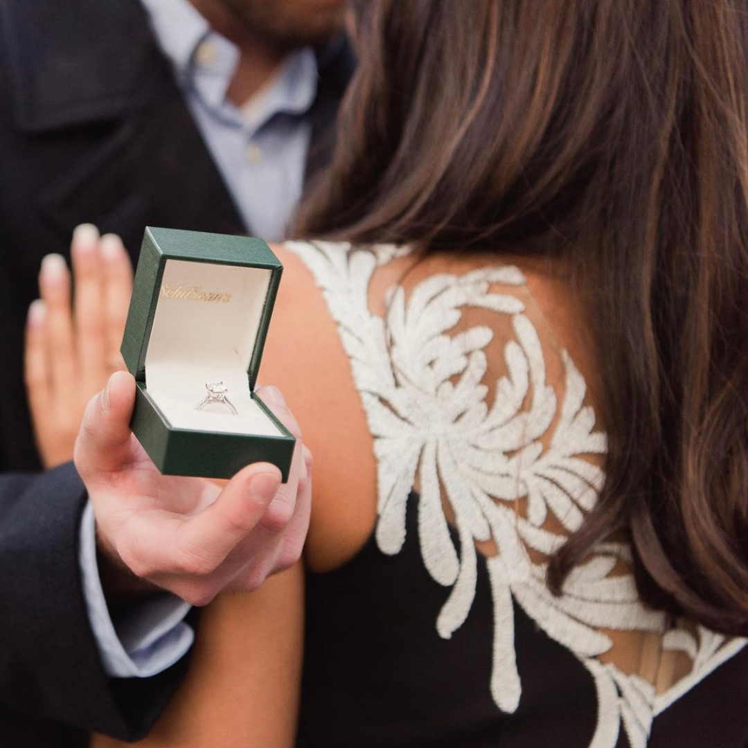 A man proposing to his girlfriend with an engagement ring in a green Schiffman's box